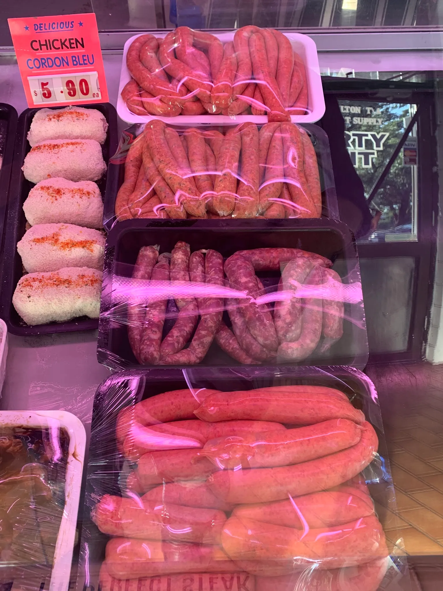 Multiple trays of sausages and frankfurts on display in a refrigerated butcher case, with a handwritten price card visible