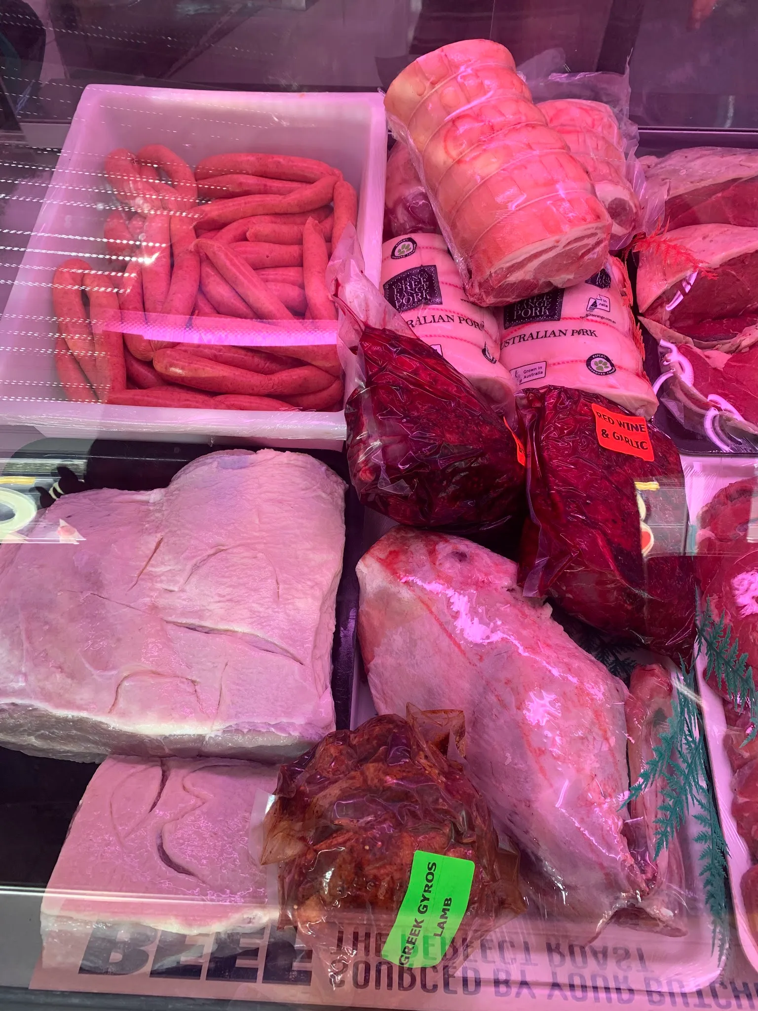 Close-up of butcher refrigerated counter showing packaged pork, sausages, and bulk cuts with a branded sticker