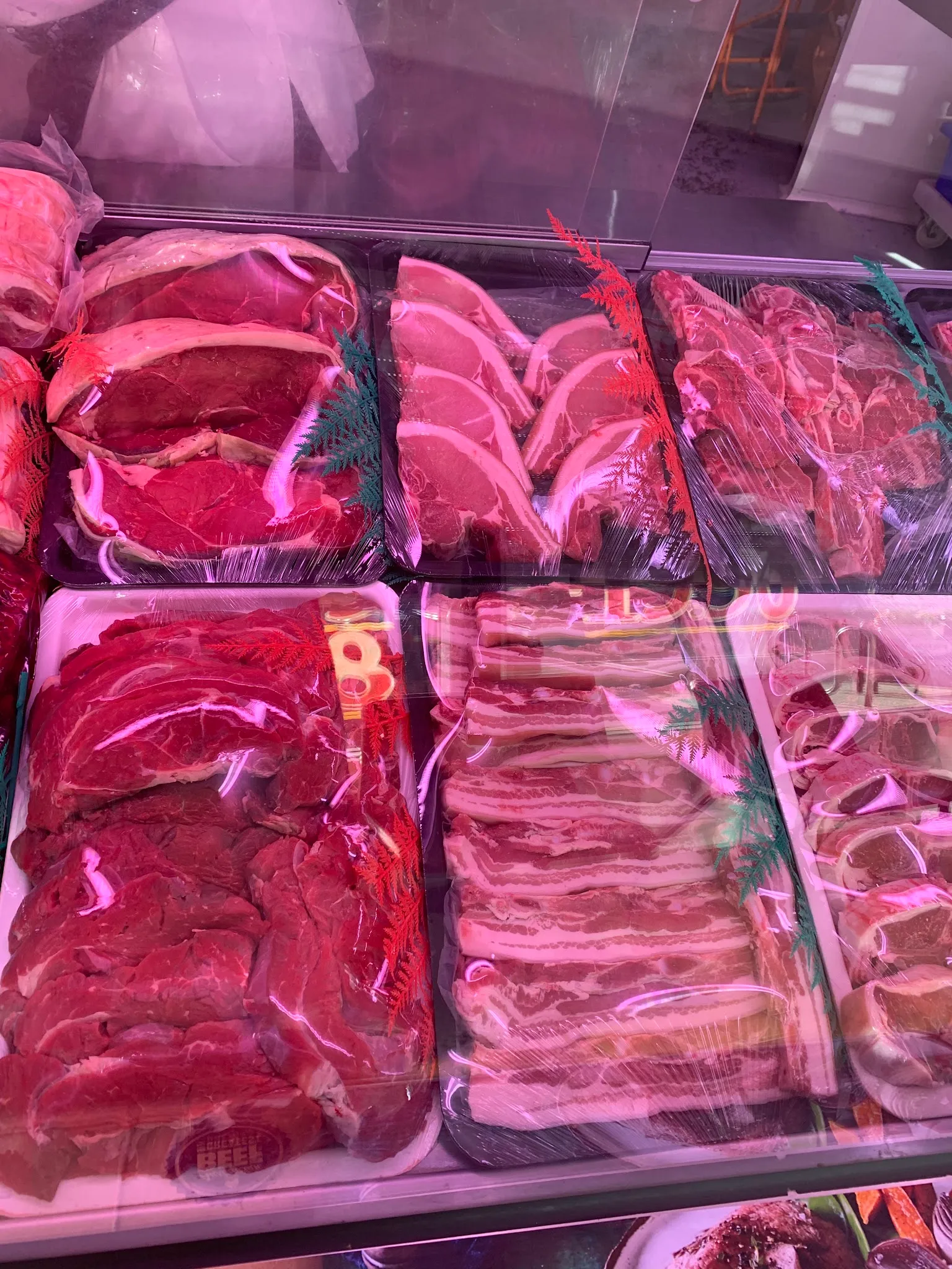 Red meat cuts including steaks, lamb chops, and bacon strips arranged in display case trays with herb garnish