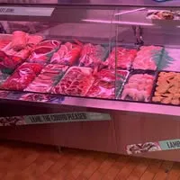 Butcher display case filled with fresh meat cuts and sausages under pink shop lighting